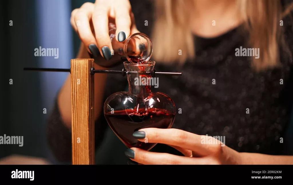 Red love potion being poured into heart-shaped bottle – romantic witchcraft love potions